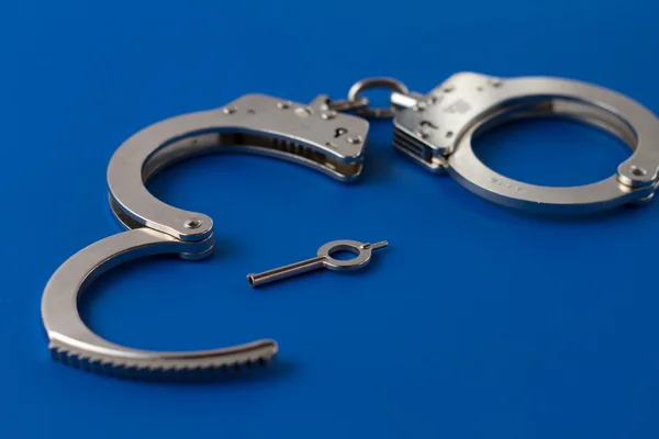 Open handcuffs with key on blue — Stock Photo, Image