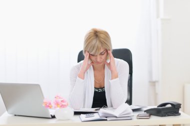 Stressed middle age business woman sitting at office table clipart