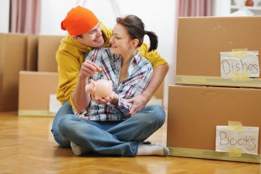 Young couple among boxes putting coin in piggy bank clipart