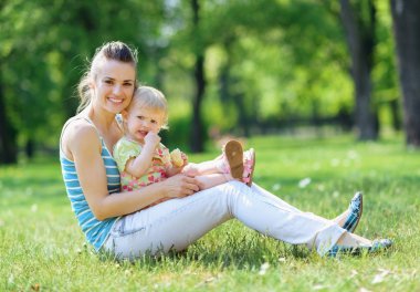 Happy mother and baby sitting on grass in park clipart