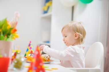 masada oturan ve doğum günü pastası yiyen bebek