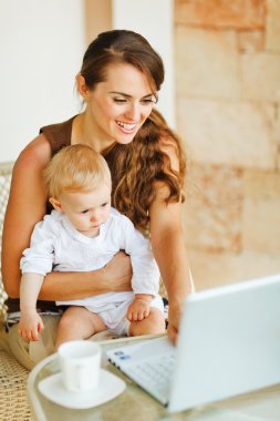 Young mother working with baby on laptop clipart