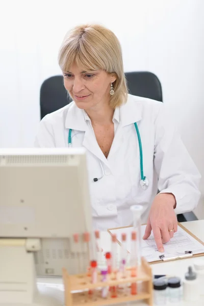 Bilgisayarda çalışan orta yaş doktor kadın gülümseyerek portresi — Stok fotoğraf