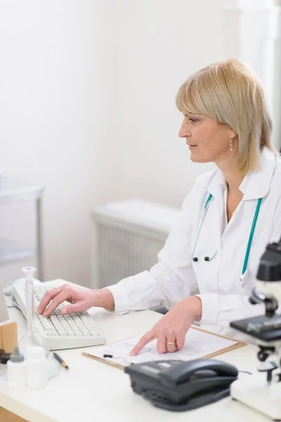 Žena středního věku lékař pracující na počítači — Stock fotografie