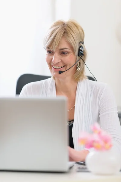 工作在笔记本电脑上的耳机的快乐高级商务女人 — 图库照片