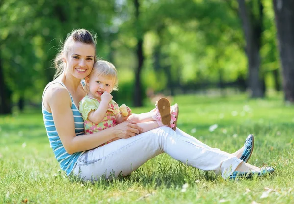 Gelukkig moeder en baby zittend op het gras in park — Stockfoto