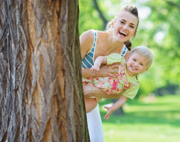 Lachende moeder en baby uitkijken van boom — Stockfoto