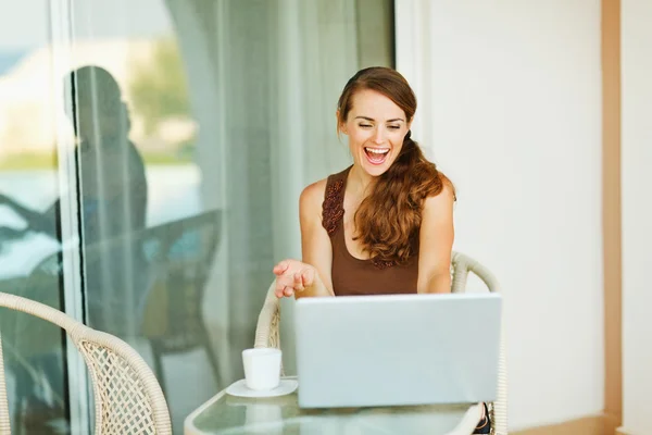 激动的年轻女子在阳台与杯咖啡在笔记本电脑上工作 — 图库照片