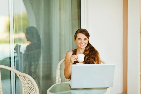 Skrattar ung kvinna njuter av kopp kaffe och tittar i laptop — Stockfoto