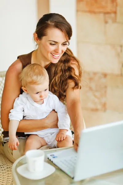 Madre joven trabajando con el bebé en el ordenador portátil — Foto de Stock