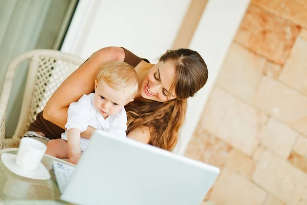 Baby zittend op moeders ronden en die op laptop werkt — Stockfoto