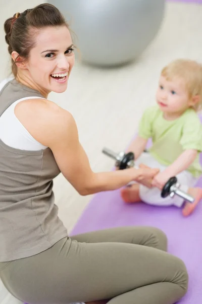 Baby helping mother lifting dumb-bell — Stock Photo, Image