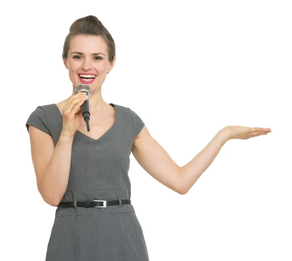 Business woman with microphone presenting something on empty hand — Stock Photo, Image