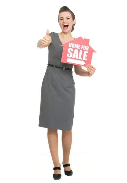 Sorrindo corretor de imóveis mostrando polegares para cima e casa para venda sinal — Fotografia de Stock