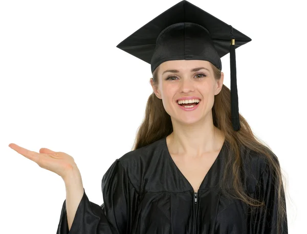 Bir şey üzerinde boş el gösterilen mezuniyet öğrenci kız gülümseyerek — Stok fotoğraf
