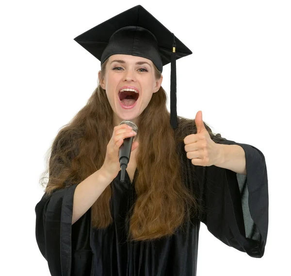 Excited graduation student girl speaking microphone and showing — Stock Photo, Image