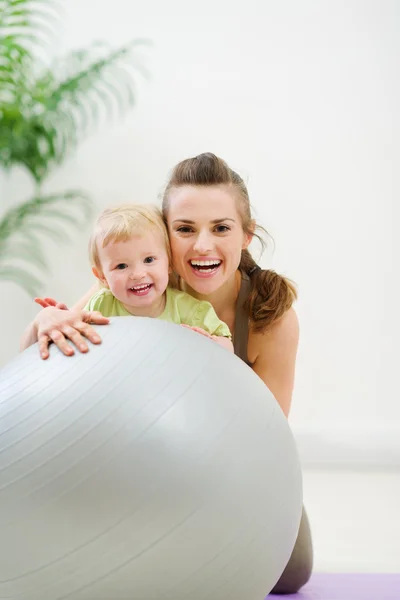 Porträt einer lächelnden Mutter und eines Babys hinter einem Fitnessball Stockbild
