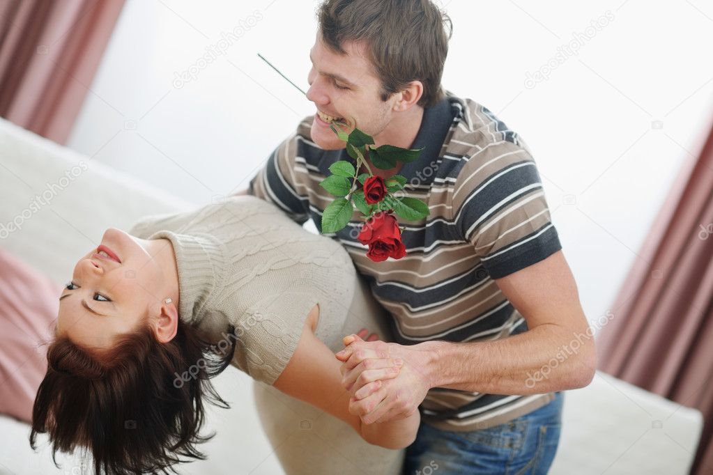 Romantic young couple dancing with red rose at home