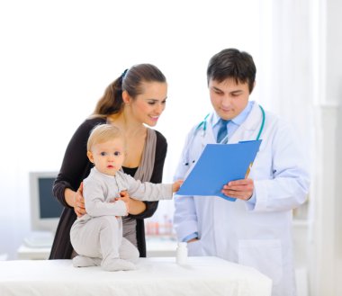 Interested baby touching patients card while pediatrician talkin clipart