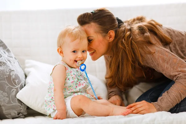 Adorable baby with soother and young mother playing on divan — Stock Photo, Image