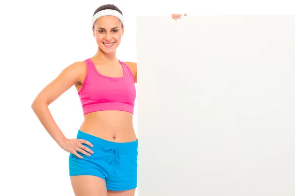 Улыбающаяся молодая девушка в спортивной одежде держит пустой рекламный щит — стоковое фото