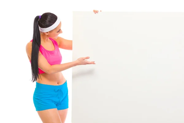 Fit girl in sportswear looking and pointing on blank billboard — Stock Photo, Image