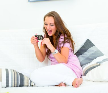 Happy pretty woman sitting on sofa and looking photos in camera clipart