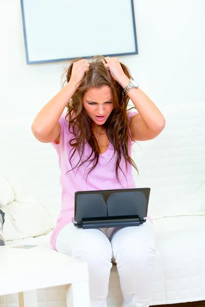 Stressed modern housewife sitting on sofa with laptop — Stock Photo, Image