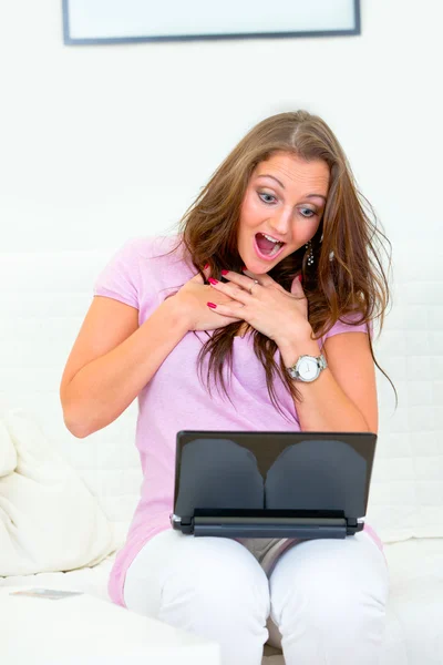 Ładna kobieta siedzi na kanapie z laptopem i amazedly patrząc na monitor — Zdjęcie stockowe
