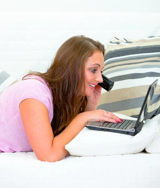 Sonriendo mujer bonita usando el ordenador portátil en el sofá y hablando por teléfono — Foto de Stock