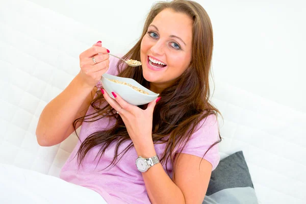 Sorrindo bela mulher sentada no sofá e comer muesli — Fotografia de Stock