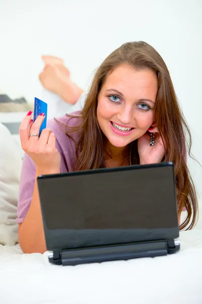 Lächelnde hübsche Frau, die auf dem Sofa liegt und mit Kreditkarte im Netz einkauft — Stockfoto