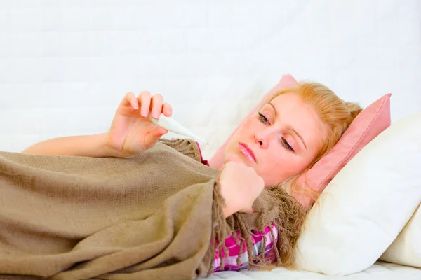 Kobieta Chora na łóżku i patrząc na termometr — Zdjęcie stockowe