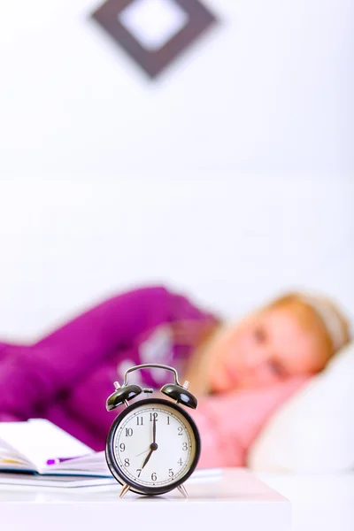 Relógio de alarme na mesa e mulher deitada no sofá no fundo — Fotografia de Stock