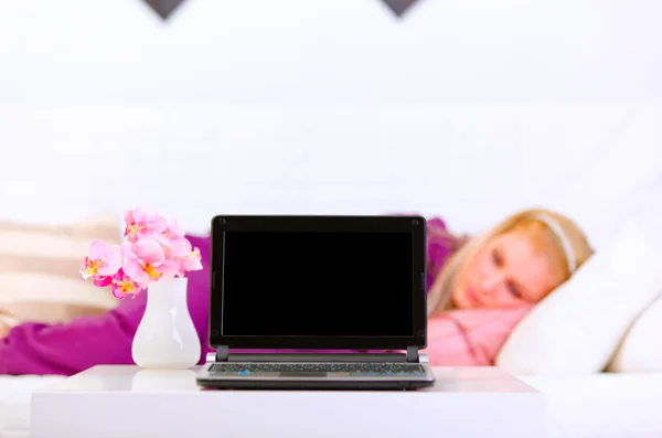 Ordenador portátil con pantalla en blanco en la mesa y la mujer acostada en el sofá en ba — Foto de Stock