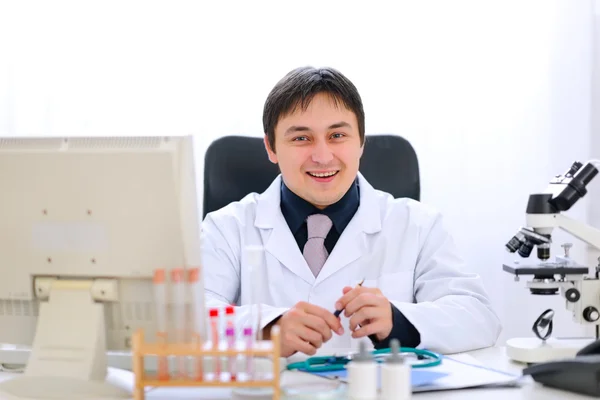 Uśmiechający się lekarz siedzi przy stole w biurze — Zdjęcie stockowe