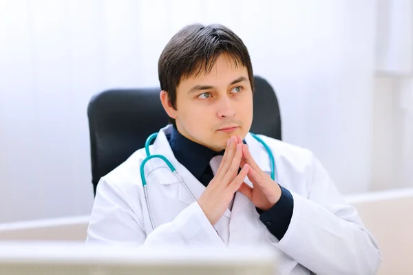 Médico reflexivo sentado en la mesa del consultorio —  Fotos de Stock
