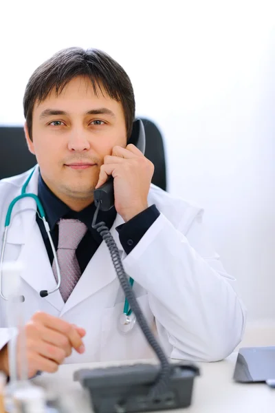 Šťastný lékař sedí u stolu v kanceláři a mluvící telefon — Stock fotografie