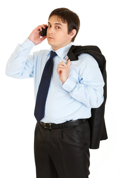 Thoughtful young businessman with jacket on his shoulder talking on mobile — Stock Photo, Image