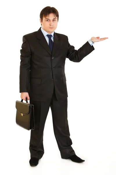 Serious businessman with briefcase presenting something on empty hand — Stock Photo, Image