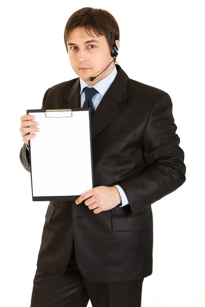 Seriöser junger Geschäftsmann mit Headset, das leeres Klemmbrett hält — Stockfoto