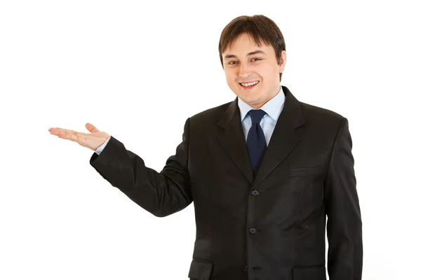 Jovem empresário sorrindo apresentando algo na mão vazia — Fotografia de Stock
