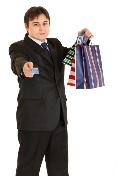 Sonriente joven hombre de negocios con bolsas de compras dando tarjeta de crédito —  Fotos de Stock