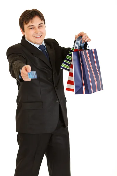 Sonriente joven hombre de negocios con bolsas de compras dando tarjeta de crédito — Foto de Stock
