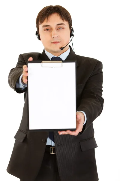 Smiling young businessman with headset holding blank clipboard — Stock Photo, Image