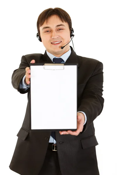 Sonriente joven hombre de negocios con auriculares sujetando portapapeles en blanco — Foto de Stock