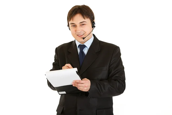 Homem de negócios moderno sorridente com fone de ouvido fazendo anotações no documento — Fotografia de Stock