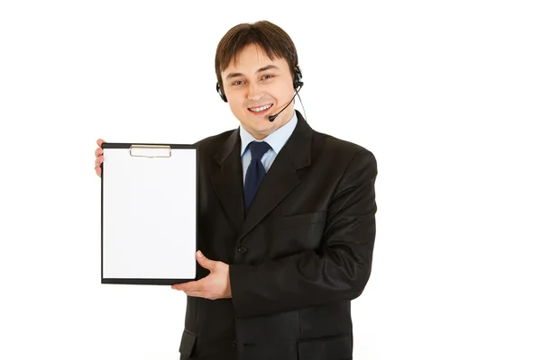 Sonriente joven hombre de negocios con auriculares sujetando portapapeles en blanco —  Fotos de Stock
