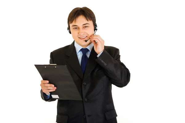 Cheerful young businessman with headset holding clipboard — Stock Photo, Image