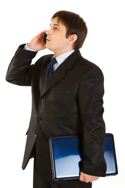 Homem de negócios moderno sério segurando laptop e falando no celular — Fotografia de Stock